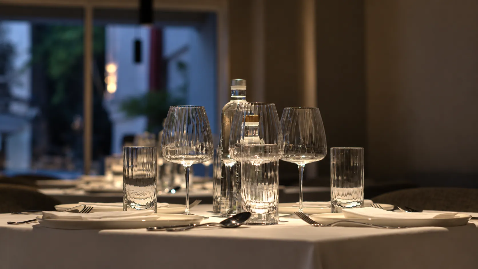 A set table at ALT with crystal glasses and a carafe in the evening light